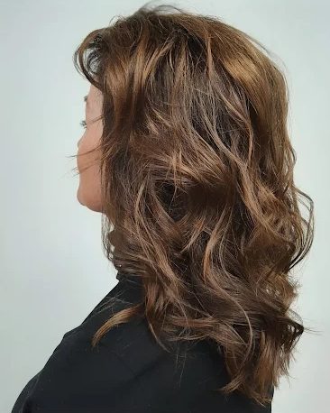 Caramel balayage on layered, waved brunette hair, shown in profile
